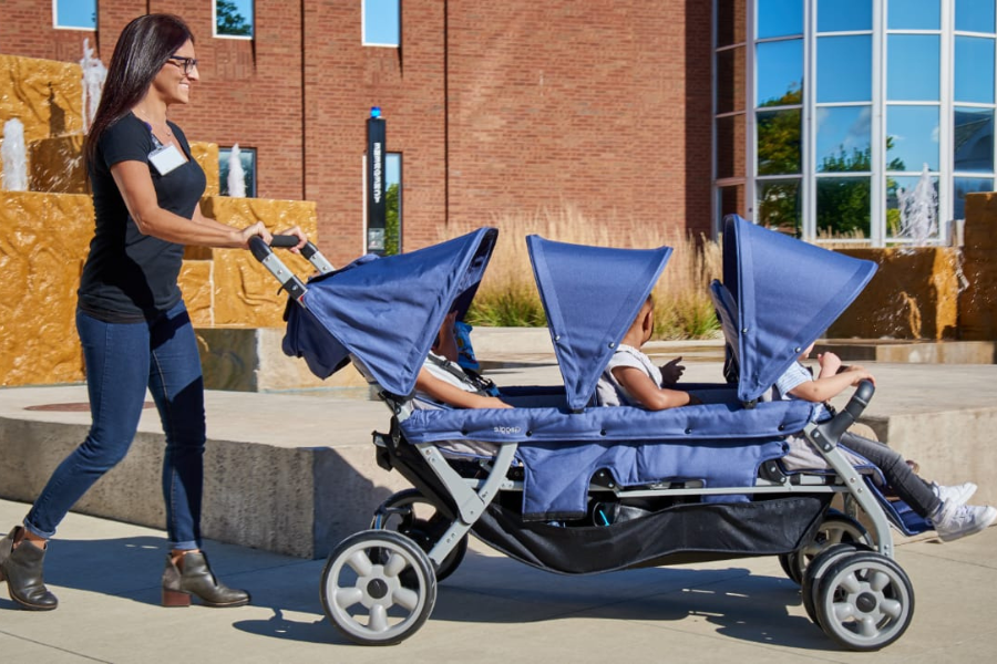 Woman pushing a stroller designed to hold six preschool aged children through a park on a sunny afternoon.. 
