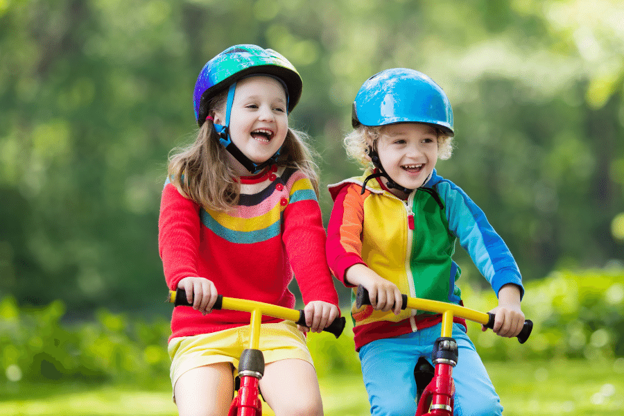 Two young preschoolers wearing helmets while riding balance bikes. 